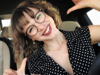 Young woman wearing glasses smiling and pointing to herself